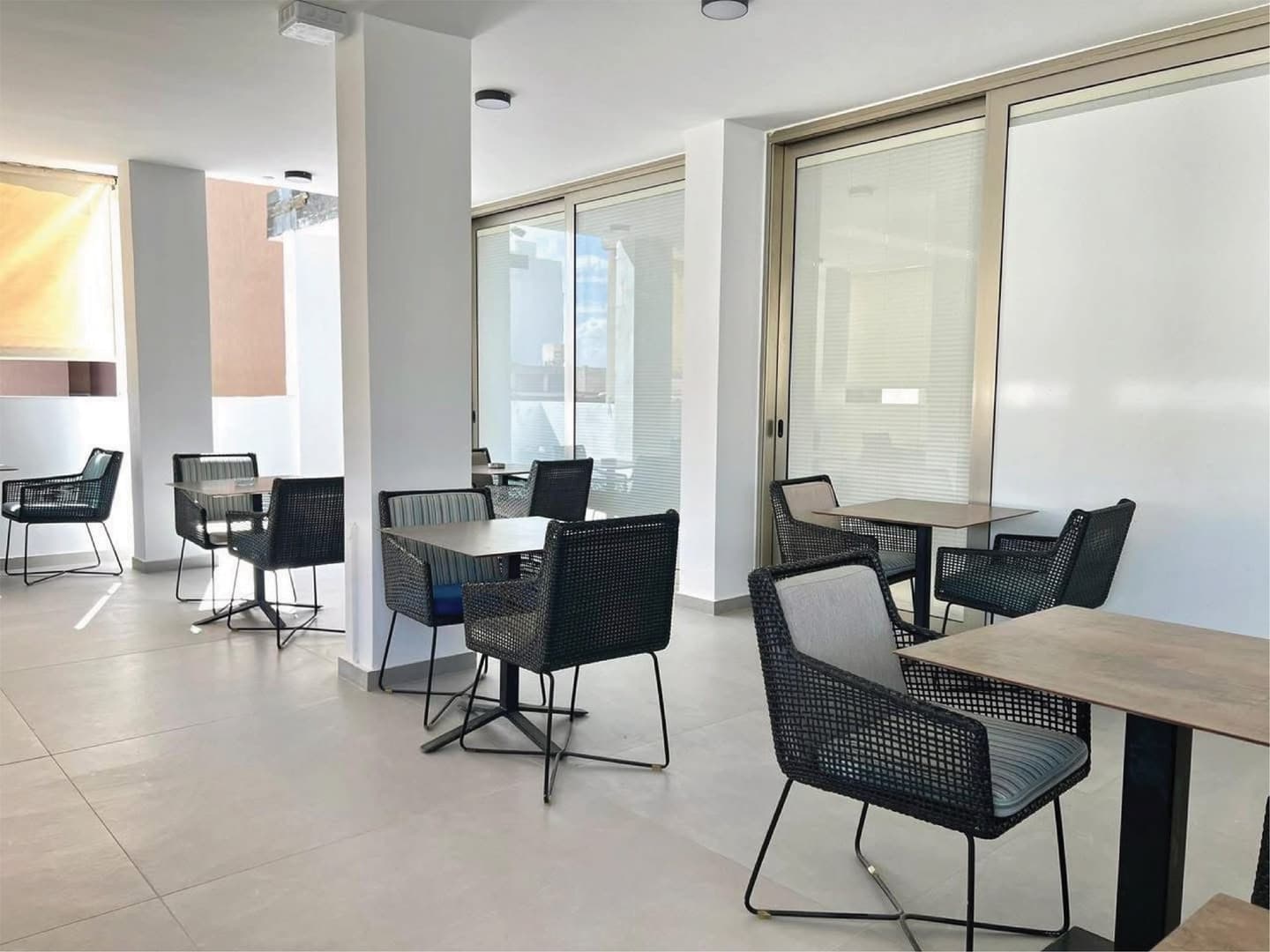 Terrace seating area with wicker chairs and small tables in a bright covered space