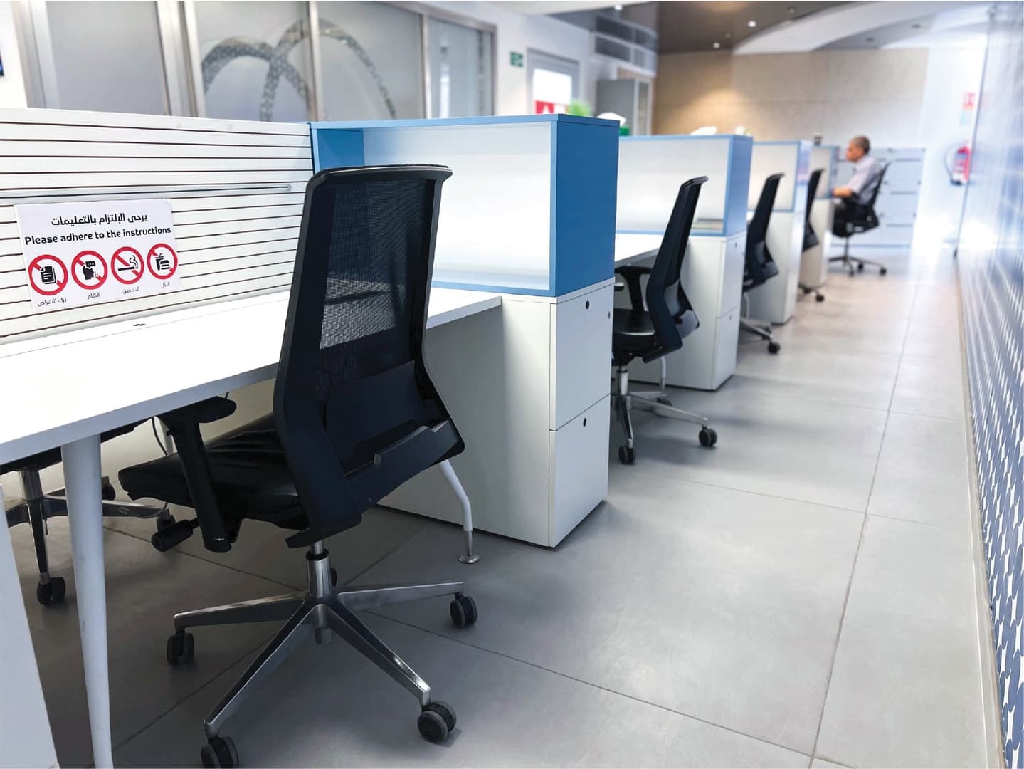 Row of workstations with blue dividers, ergonomic chairs, and bilingual instruction signs