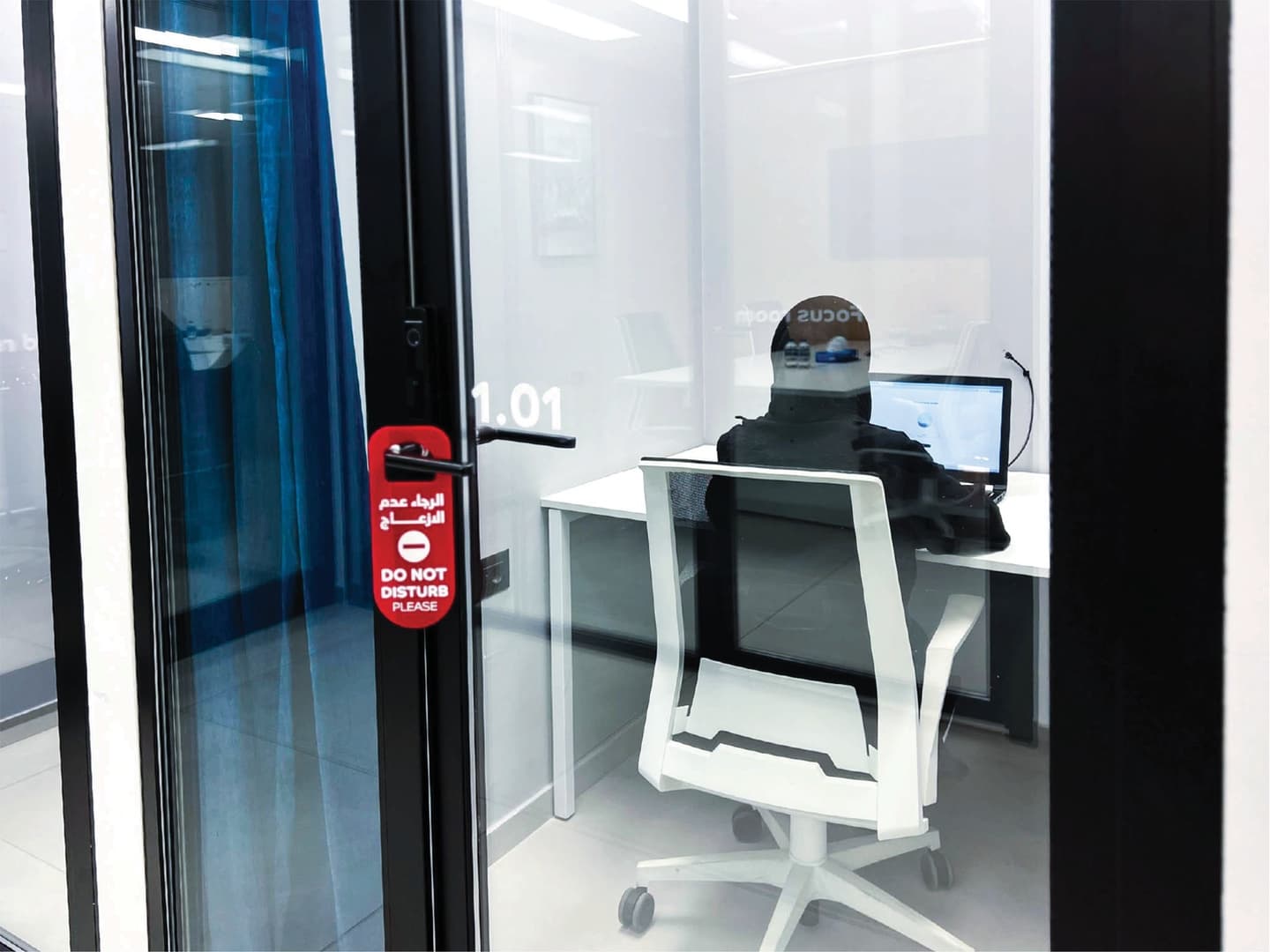 Single Room - person working at desk with monitor, viewed through glass door